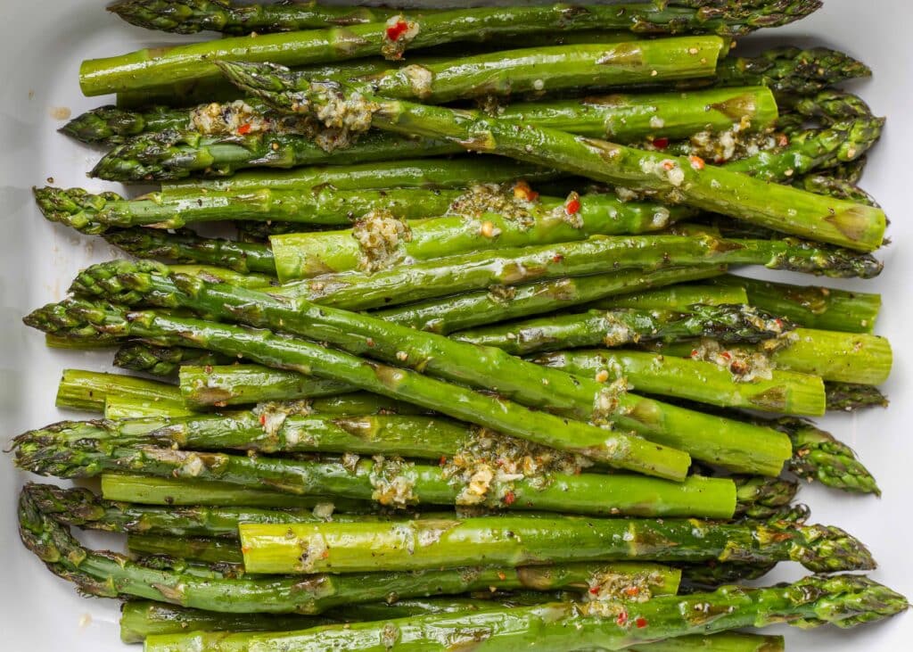 a close up shot of asparagus spears in a white baking dish.