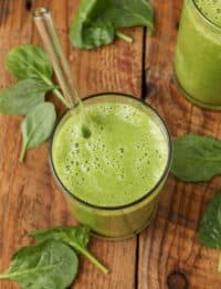 a top down shot of a banana spinach smoothie on a wooden tabletop with spinach leaves arranged around it
