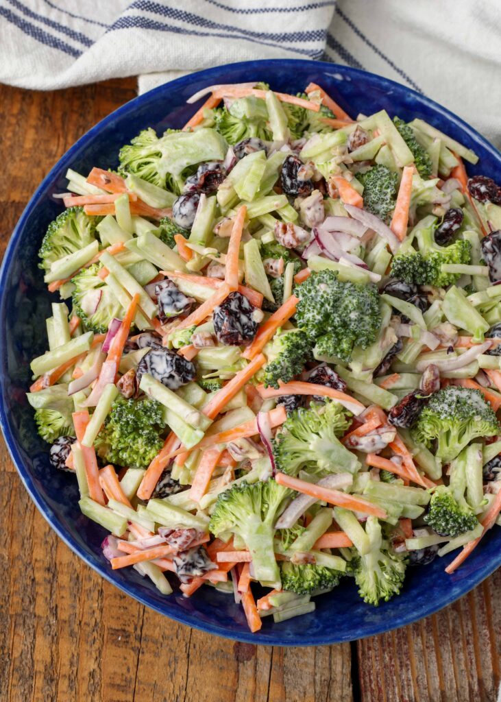 broccoli slaw in blue bowl on wooden table with cloth