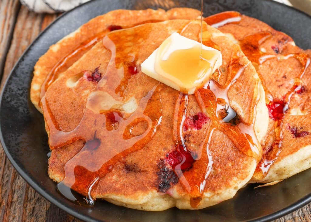 pancakes with cranberries, butter, and syrup on black plate