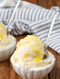 A scoop of lemon curd ice cream is nestled in a small white bowl with a long handled metal spoon sticking out