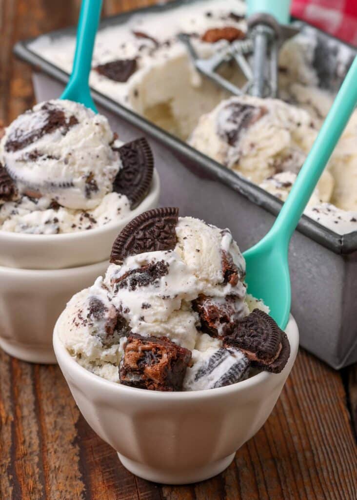 Chunks of cookie and brownie have been scattered atop the bowls of ice cream with a green spoon.
