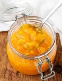 Overhead shot of peach sauce in a glass jar, served with a silver spoon