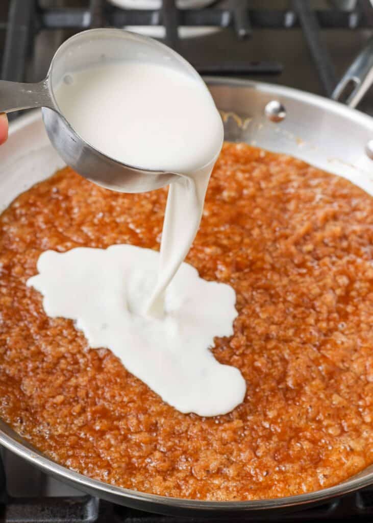 Overhead shot of cream and caramelized praline mixture in a stainless steel skillet