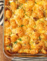 The tater tot breakfast casserole has come out of the oven and is crispy brown on the edge with gooey melted cheese on top.