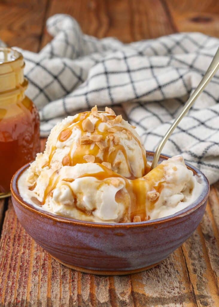 Toffee ice cream topped with caramel syrup and toffee bits, served with a silver spoon