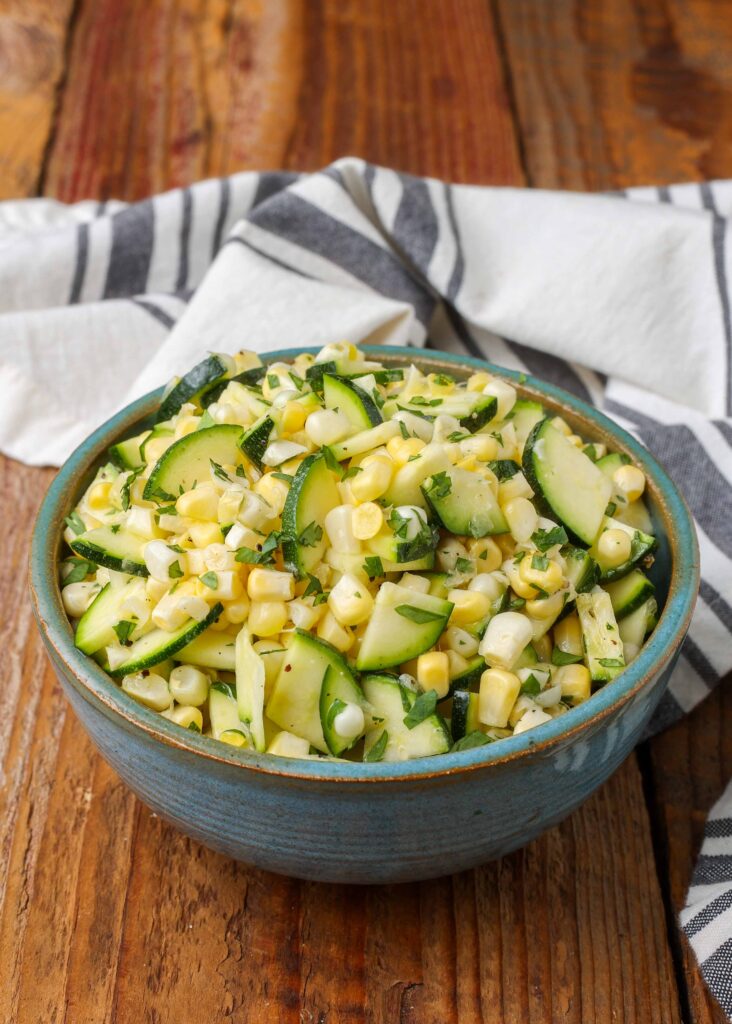 Zucchini corn salad, served in a small blue ceramic bowl with a striped gray and white towel